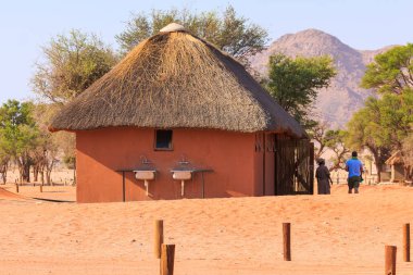 Sesriem Kampı, Sossusvlei, Namibya - 01 Ekim 2018: Kamp alanındaki insanlar. Arka tarafında sazdan bir çatı dağı olan bir bina. Cihazları yakınlarda park edilmiş bir araba..