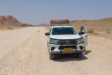 Sesriem, Naukluft, Namibya - 01 Ekim 2018: Namibya 'daki tipik 4x4 kiralık araba kamp malzemeleri ve Namibya çöllerinde toprak bir yolda ilerleyen bir çatı çadırı.