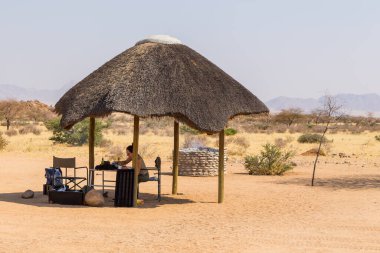 Solitaire, Namibya - 01 Ekim 2018: Solitaire Çöl Çiftliği 'nin kamp alanındaki çardakta oturan bir kız. Savanna arka planda.