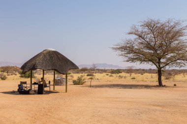 Solitaire, Namibya - 01 Ekim 2018: Solitaire Çöl Çiftliği 'nin kamp alanındaki çardakta oturan bir kız. Savanna arka planda.