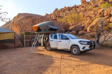 Mowani, Damaraland, Namibya - 04 Ekim 2018: Namibya 'da kamp malzemeleri ve kamp alanında bir çatı çadırıyla donatılmış tipik 4x4 kiralık araba.