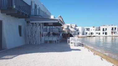 Naoussa, Paros Adası, Yunanistan - 27 Eylül 2020: Paros adasındaki küçük liman kasabasının manzarası. Kıyıdaki beyaz villalar. Küçük sahildeki restoranda insanlar var..