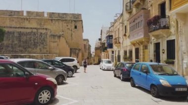 Birgu, Malta - 21 Haziran 2021: Malta 'da güneşli bir günde Birgu' da bir sokakta yürümek. Arabalar park yerinde. İki taraftaki eski binalar..