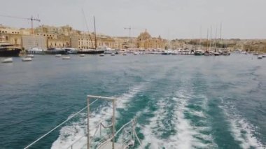 Birgu, Malta - 21 Haziran 2021: Malta 'da Birgu ve Valletta arasında feribota binmek. Yat limanda demirli. Feribotla uyanma ve köpük. Arka planda Birgu kasabası var..