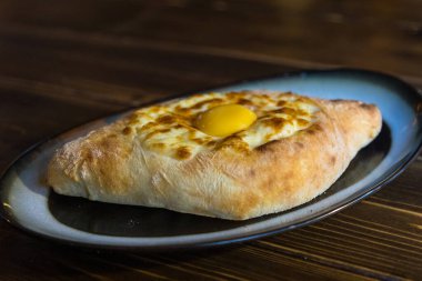 Adjarian Khachapuri - geleneksel Gürcü mutfağı. Peynirli, tereyağlı ve yumurtalı pişirmeye hazır siyah tabakta.