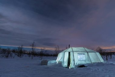 Karlı açıklıkta hafif bir çadır, arka planda dağlar. Bulutlu bir akşam. Abisko, Laponya, İsveç.