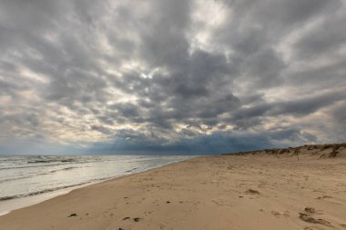 İsveç 'in güneyindeki Sandhammaren plajında dramatik bulutlu gökyüzü altında çimenli sahil kum tepeleri..