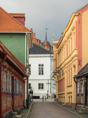 Ystad, İsveç - 7 Mart 2020: Dar kaldırımlı, renkli eski binalar ve tarihi şehir merkezindeki kule.