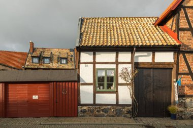 Ystad, İsveç - 7 Mart 2020: Çatı döşemesi, yeşil pencere ve sessiz bir caddedeki kırmızı garajlı tarihi yarı keresteli ev.