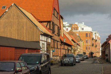 Ystad, İsveç - 7 Mart 2020: Bulutlu gökyüzü altında park edilmiş arabaları ve tarihi tuğla mimarisi olan bir kaldırım taşı caddesi.