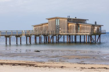 İsveç 'in Torekov sahilinde tahta ayaklıklar üzerinde ahşap sahil hamamı. Bulutlu gökyüzü ve alçak gelgitle sakin bir gün.