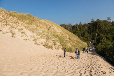 Leba, Polonya 12 Eylül 2020: Turistler Slowinski Ulusal Parkı 'ndaki kum tepeleri yakınında çitli bir patika boyunca yürüyorlar.