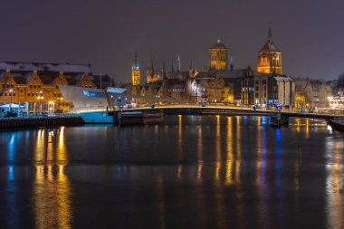 Gdansk, Polonya 2 Şubat 2021: Tarihi kiliseler ve eski kasaba silueti gece aydınlık bir yaya köprüsü ile görülüyor.