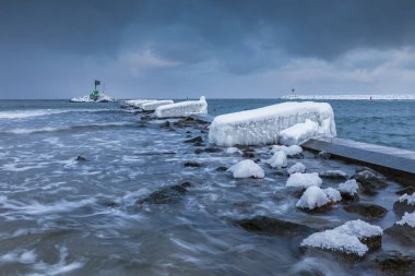Gorki Zachodnie, Gdansk, Polonya 'daki Baltık Denizi' nde buzla kaplı kayalar ve dalgakıranlar. Deniz feneriyle kışın deniz manzarası.
