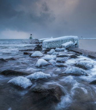 Gorki Zachodnie, Gdansk, Polonya 'daki Baltık Denizi' nde buzla kaplı kayalar ve dalgakıranlar. Deniz feneriyle kışın deniz manzarası.