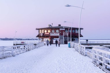 Puck, Polonya 13 Şubat 2021: İnsanlar alacakaranlıkta bir ahşap restorana giden karla kaplı iskelede yürüyor.