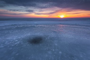 Polonya 'da Chalupy yakınlarında gün batımında donmuş Baltık Denizi, parlak turuncu gökyüzü ve ön planda buz dokusu ile.
