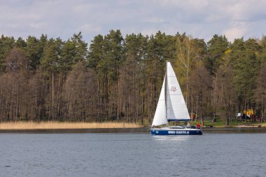 Rydzewo, Polonya - 01 Mayıs 2021: Bulutlu gökyüzünün altındaki Mazury göllerindeki bir yelkenli yarışı sırasında beyaz ve mavi yelkenliler.