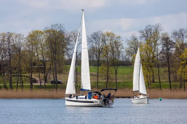 Rydzewo, Polonya - 01 Mayıs 2021: Bulutlu gökyüzünün altındaki Mazury göllerindeki bir yelkenli yarışı sırasında beyaz ve mavi yelkenliler.