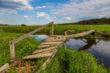 Polonya 'nın Odrynki köyü yakınlarında eski ahşap bir köprü sakin bir nehri geçer. Bir yaz gününde huzurlu kırsal manzara.