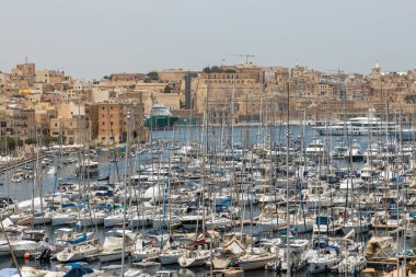 Birgu, Malta - 21 Haziran 2021: Arka planda Birgu 'nun tarihi şehir manzarası olan kalabalık bir yat ve yelkenli marina manzarası.