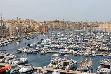 Birgu, Malta - 21 Haziran 2021: Arka planda Birgu 'nun tarihi şehir manzarası olan kalabalık bir yat ve yelkenli marina manzarası.