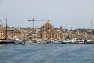 Birgu, Malta - 21 Haziran 2021: Birgu 'daki tarihi mimari ve balkonlarla rıhtım boyunca yüzen ve kenetlenen teknelerin görüntüsü.
