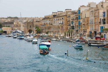 Birgu, Malta - 21 Haziran 2021: Birgu 'daki tarihi mimari ve balkonlarla rıhtım boyunca yüzen ve kenetlenen teknelerin görüntüsü.