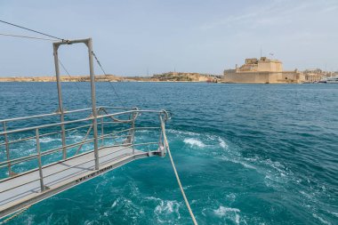 Valletta, Malta 21 Haziran 2021: Geleneksel bir teknede limanda kırmızı bir gölgelik, arka planda tarihi binalar ve yatlar olan bir adam.