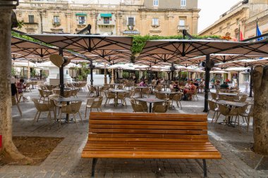 Valletta, Malta 21 Haziran 2021: Polis arabaları, eski binalar, balkonlar ve Valletta tarihi merkezinde yürüyen bir kadın ile dar eğimli cadde.