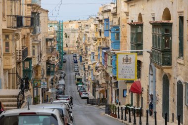 Valletta, Malta 21 Haziran 2021: Polis arabaları, eski binalar, balkonlar ve Valletta tarihi merkezinde yürüyen bir kadın ile dar eğimli cadde.