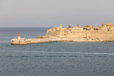 Taştan iskelenin sonundaki kırmızı çatılı deniz feneri Valletta, Malta Akdeniz kıyısındaki antik bir kale duvarının yanında..