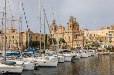 Birgu, Malta 21 Haziran 2021: Tarihi mimari ve kilise kuleleri manzaralı yat ve tekneler limana demir attı.