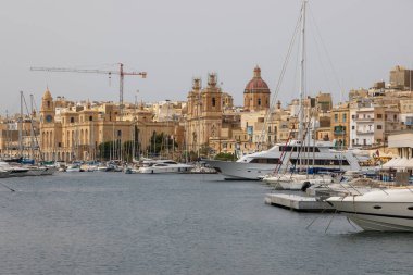 Birgu, Malta 21 Haziran 2021: Tarihi mimari ve kilise kuleleri manzaralı yat ve tekneler limana demir attı.