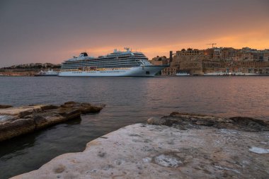 Valetta, Malta 21 Haziran 2021: Şehir ışıklarının ve ön plandaki kıyı kayalarının yansımalarıyla huzurlu bir gece..
