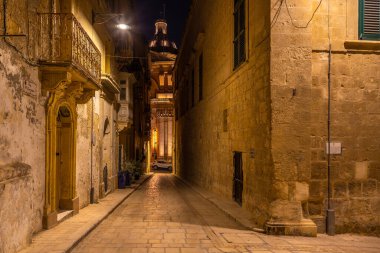 Birgu, Malta 21 Haziran 2021: Sıcak ışık altında saksı bitkileri ve kireçtaşı binaları olan sessiz bir sokak.