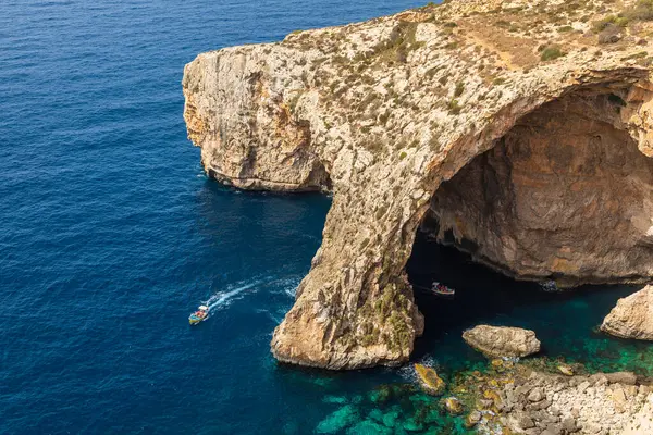 Blue Grotto, Malta 22 Haziran 2021: Turist tekneleri engebeli kireçtaşı kıyılarında geniş bir doğal kemer oluşumuna yaklaşıyorlar.
