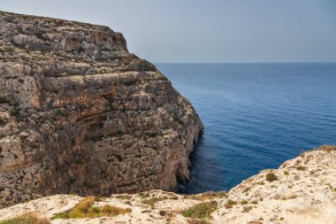 Malta 'da Blue Grotto yakınlarındaki sarp kayalıklar sakin mavi deniz ve yaz ışığında kuru kıyı arazisi.