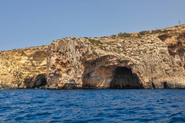Malta 'daki Blue Grotto sahilindeki dramatik deniz kayalıkları ve doğal mağaralar. Açık gökyüzü ve mavi su.