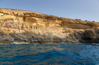 Blue Grotto, Malta 'da renkli katmanlı kaya oluşumları ve turkuaz deniz. Sahilde güneşli bir gün.