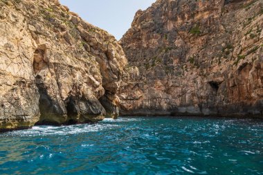 Malta 'daki Blue Grotto yakınlarında kayalık kayalıklar berrak turkuaz suların üzerinde yükselir. Parlak güneşli hava.