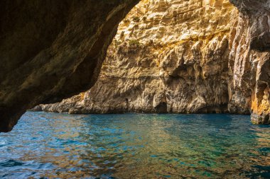 Güneş ışığı, Malta, Blue Grotto 'daki bir kıyı mağarasında dokulu kaya duvarlarını aydınlatır. Turkuaz suyu temizle.