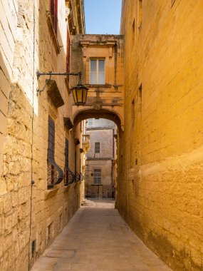 Malta 'nın tarihi Mdina şehrinde kemer ve fenerli dar bir taş sokak..
