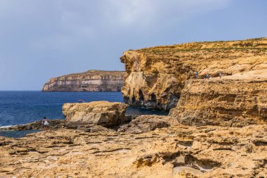 Gozo, Malta 23 Haziran 2021: Turistler Akdeniz 'e bakan engebeli kireçtaşı kayalıklarını keşfediyorlar.