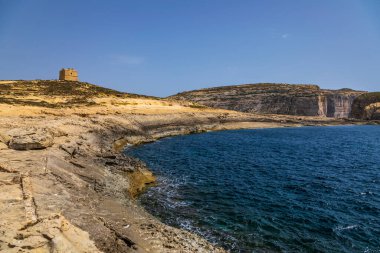 Taş gözetleme kulesi engebeli kayalık sahil şeridi ve Gozo Malta 'daki derin mavi Akdeniz suları..
