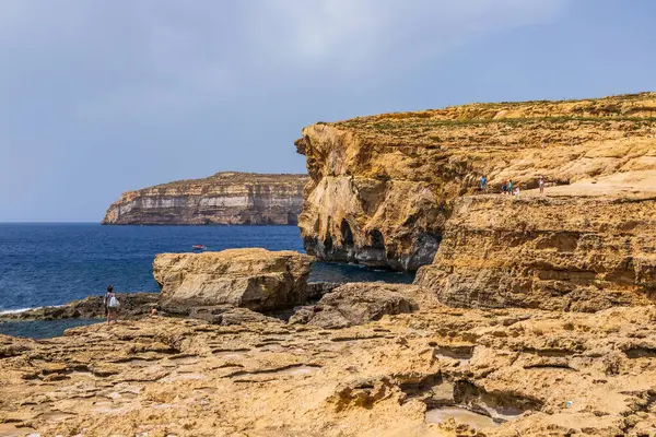 Gozo, Malta 23 Haziran 2021: Turistler Akdeniz 'e bakan engebeli kireçtaşı kayalıklarını keşfediyorlar.