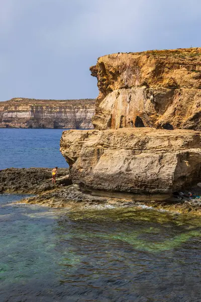 Gozo, Malta 23 Haziran 2021: Turistler Akdeniz 'e bakan engebeli kireçtaşı kayalıklarını keşfediyorlar.