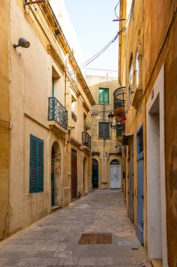 Gozo, Malta 23 Haziran 2021: Victoria 'da dar kireçtaşı sokağı eski taş duvarlar ve geleneksel Malta mimarisi ile çevrili yeşil ahşap kapının önünde park etmiş bir scooter ile..