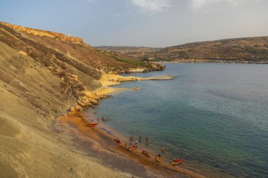 Manikata, Malta 24 Haziran 2021: Turkuaz sular ve çevre tepelerle Golden Bay sahilinde dinlenen turistler.