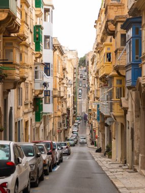 Valletta, Malta 26 Haziran 2021: Valletta, Malta 'da geleneksel Malta balkonlarının yer aldığı arabalar ve tarihi evlerle dolu dar bir cadde.